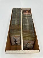 Box containing a large quantity of vintage baseball cards, each individually sleeved in protective plastic cases, showing black and white or sepia-toned images of players.