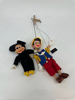 Photo of both Disney marionette puppets, Mickey Mouse and Pinocchio, with string control bars visible