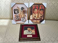 Group shot of all three framed baseball pictures on a patterned cloth surface, two large pieces with protective corner covers, one smaller framed photo in front.