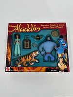 Front of Mattel Disney Aladdin action figure playset box showing Jasmine, Rajah tiger, Genie, magic lamp, cage, and coin figures and accessories.