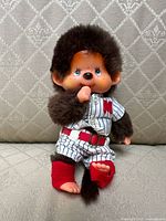Front view of Monchhichi doll wearing baseball uniform sitting on a patterned cushion.