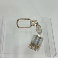 Silver rectangular keychain with 18k gold accent lines on a transparent display stand, front view showing gold bands.
