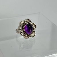 Front angled view of silver ring with prominent oval cabochon amethyst stone and floral silver design surrounding it.