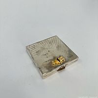 Closed compact front showing sunburst guilloche pattern and bow clasp