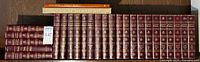 Photo showing the full set of 23 Encyclopedia Britannica volumes arranged side by side with two atlases stacked on top.