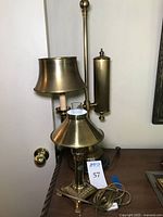 Photos showing two vintage brass table lamps on a wood surface, one tall with fabric shade and reservoir, the other smaller with glass chimney and reflector shade.