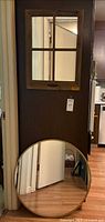 Wall display of two mirrors hanging on a wall. The upper item is a square mirror with wooden frame divided into six sections. Below is a round mirror with wooden rim, reflecting part of room and floor.