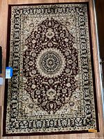 Full view of rectangular area rug with burgundy medallion on beige and black floral background, showing detailed pattern and size.