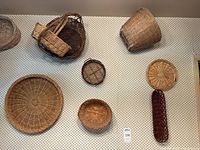 View of larger round and shallow baskets along with small and medium round baskets and an elongated dark brown handled basket all hanging on patterned wallpaper.
