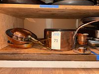 Shelf photo showing stacked copper pans, a large pot, and small burner stand with copper pieces.