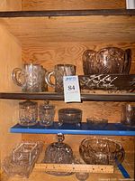 View of several clear cut glass items including two mugs, two lidded candy jars, a round dish on feet, small round bowl, rectangular divided dish, covered butter dish, and a large bowl.