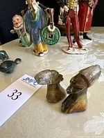 Pair of stone-carved bust figurines with visible facial features and headwear shown alongside other assorted figurines.