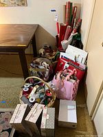 Photo of a corner showing various wrapping paper rolls in plaid and other patterns, baskets filled with ribbons and smaller gift bags, and additional bags standing upright.