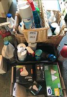 Photo showing two woven baskets filled with assorted cleaning products and spray bottles, along with multiple unopened LED light bulbs and related lighting items in original packaging placed in front.