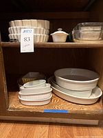 Shelf view of stacked white oval and round ceramic baking dishes, clear glass baking dishes, and white butter dish.