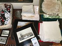 Stack of assorted linens including embroidered napkins, crochet doilies, and woven placemats with square coasters showing architectural prints