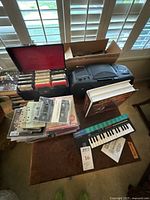 Wide view of lot on table showing cassette tapes in cases and loose, vinyl records, Sony portable CD player, and Casio keyboard.