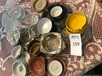 Top view of assorted vintage ashtrays showing variety of styles and colors on lace tablecloth, includes glass, ceramic and metal pieces