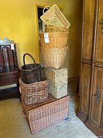 Stacked assortment of 11 wicker and woven baskets of varying size and color, showing range and handles visible.