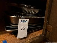 Stack of baking sheets, roasting pans, and cooling racks seen from the side, showing materials and quantity.