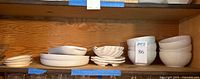 Shelf with stacked white ceramic bowls and plates including Pfaltzgraff and assorted shapes