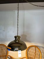 Full view of brass pendant light hanging by chain with rattan chairs in background, showing overall shape and finish