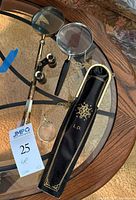 Photo showing all items together: Brookstone opera glasses, ornate magnifying glass, magnifying glass pendant with chain, and monogrammed case.