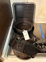 Overall collection of cast iron cookware on stove including griddle, frying pans, grill/press and ladle