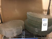 Stack of clear glass plates on a metal shelving unit with a label showing lot number 122