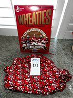 Front view of the red Wheaties cereal box featuring the San Francisco 49ers and the Super Bowl XXIX championship players with the red 49ers sweatpants below featuring repeating team logos.