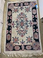 Full view of the floral cream colored wool area rug with black border and fringed edges