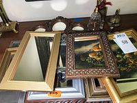 Photo showing stacked framed mirrors with various decorative frames in gold, silver, and wood finishes alongside a glass bell and metal bell.