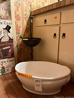 Ceramic planter and metal birdbath set displayed together near cabinetry with visible measuring sticker and lot number tag.