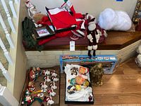 Wide view of assorted Christmas decoration items including boxes with fabric and ceramic ornaments, train set box, and tree skirts.