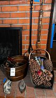 Photo of entire lot including copper bucket, brass coal scuttle filled with pine cones, iron tongs, natural broom, bellows, matches, and lighter.