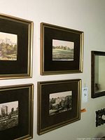 Four framed art prints depicting castles and landscapes hung on a wall, showing the gold-toned frames and dark brown mats.