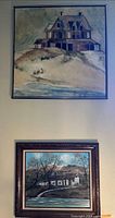Two framed artworks hanging on wall, including a beach house scene and rustic cabin painting