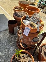 Terracotta planters arranged outside with soil and dried plants, including one planter with metal mesh piece inside.