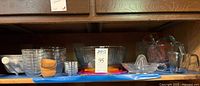 Shelf view showing glass bowls, Pyrex measuring cups, wooden bowls, and glass citrus juicer. All items arranged neatly.