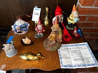 Overview of the gnomes figurines arranged on a wooden table alongside brass duck decorations and a certificate.