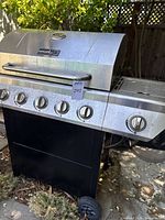 Nexgrill propane gas grill showing five main burners, one side burner, black body and wheels