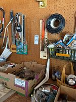 Photo showing hand saws, hardware items, and extension cord coil on pegboard with cardboard boxes of tools below.