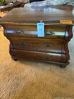 Front and angled view of the wooden dresser showing three spacious drawers with ornate metal handles and curved front design.