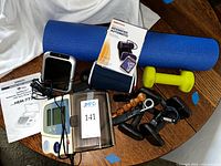 Full lot view showing yoga mat rolled up blue, pair of yellow 5 lb dumbbells, hand grips, two blood pressure monitors, manual and wrist cuffs for monitors.