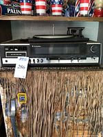 Full front view of stereo console showing turntable on top, control panel with buttons and knobs, AM/FM radio tuning dial, 8-track player slot, headphone jack, and woodgrain cabinet.