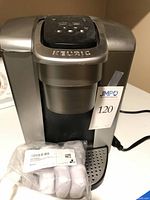 Front view of Keurig K-Elite coffee maker with included sealed bag of coffee filters on drip tray.