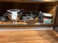 Overview of stainless steel kitchen tools and gadgets on wooden shelf, including bowls, strainers, colanders, grater, and measuring cup.