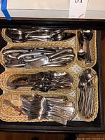 Six small wicker baskets holding grouped stainless steel utensils: forks, spoons, knives and serving pieces.