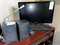 Photo of LG Flatron monitor, Mitsubishi speakers, wired keyboard and white based microphone on a wooden table