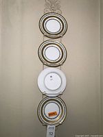 Vertical view of four Limoges porcelain plates with green and gold wreath borders shown on a metal rack, three plates front side up and one plate backside shown with manufacturer's marks.